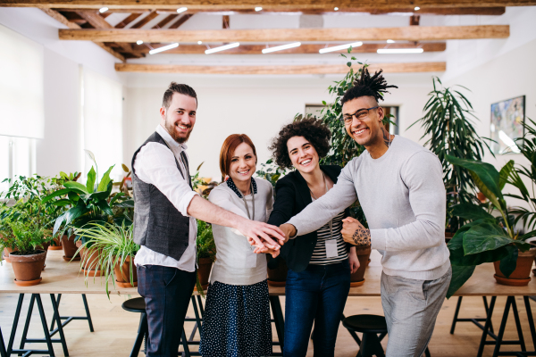 A group of young businesspeople standing in office, putting hands together.