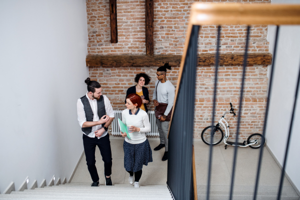 Group of young businesspeople walking up the stairs in indoors, talking. A start-up concept.