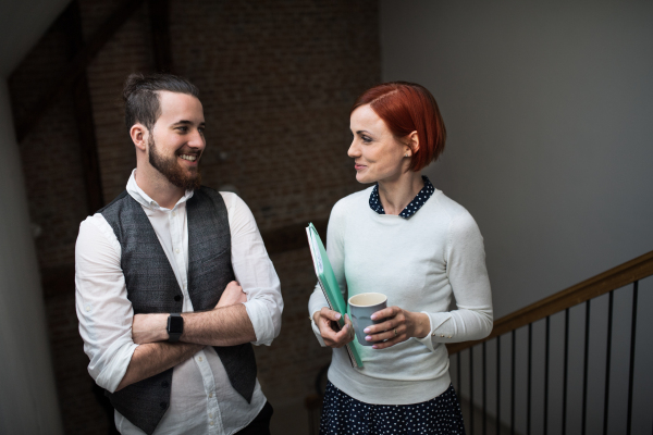 Two young businesspeople walking up the stairs in indoors, talking. A start-up concept.