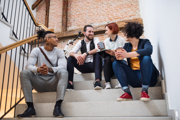 Group of young businesspeople sitting on stairs indoors, talking. A start-up concept.