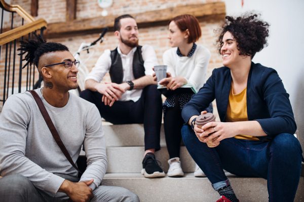 Group of young businesspeople sitting on stairs indoors, talking. A start-up concept.