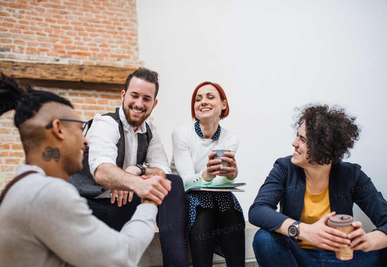 Group of young businesspeople sitting on stairs indoors, talking. A start-up concept.