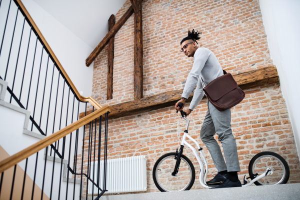 A young mixed race businessman with scooter in office building.