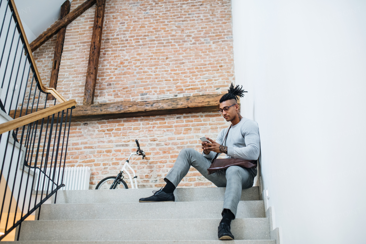 A young mixed race businessman with telephone sitting on stairs in office building.