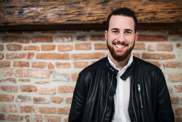 A happy young businessman standing outdoors against brick wall. Copy space.