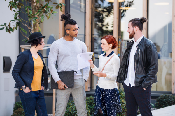 Group of young businesspeople standing outdoors in courtyard, talking. A start-up concept.