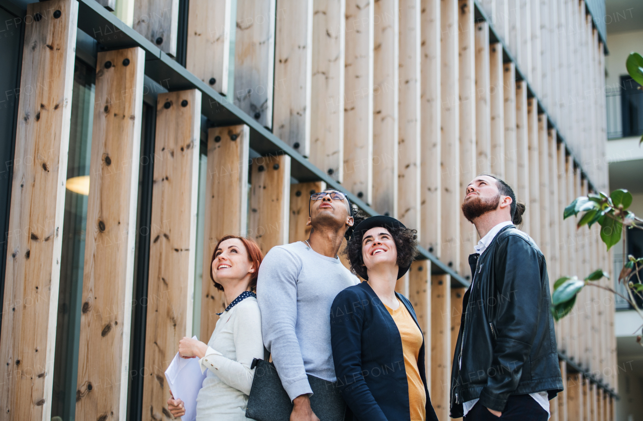 Group of young businesspeople standing outdoors in courtyard, looking up. A start-up concept.