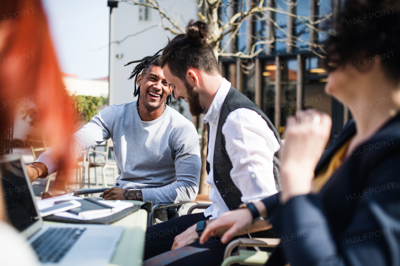 Young businesspeople with laptop outdoors in courtyard, laughing. Start-up concept.