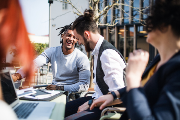 Young businesspeople with laptop outdoors in courtyard, laughing. Start-up concept.