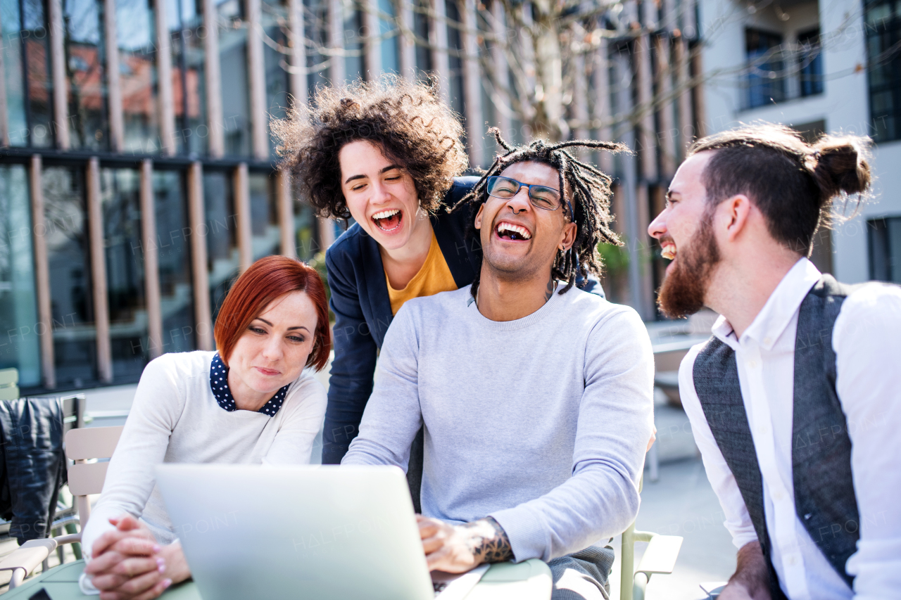 Young businesspeople with laptop outdoors in courtyard, laughing. Start-up concept.