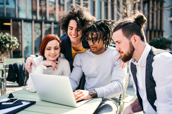 A group of young businesspeople using laptop outdoors in courtyard, start-up concept.