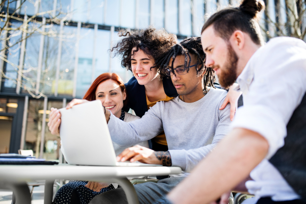 Young businesspeople with laptop outdoors in courtyard, laughing. Start-up concept.