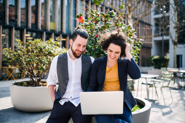 Young businesspeople with laptop outdoors in courtyard, working. Start-up concept.