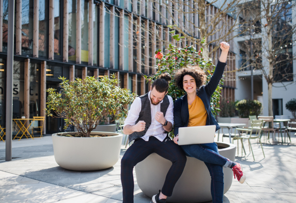 Young businesspeople with laptop outdoors in courtyard, expressing excitement. Start-up concept.