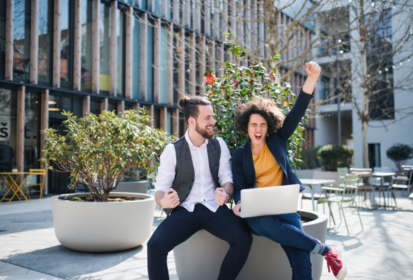 Young businesspeople with laptop outdoors in courtyard, expressing excitement. Start-up concept.