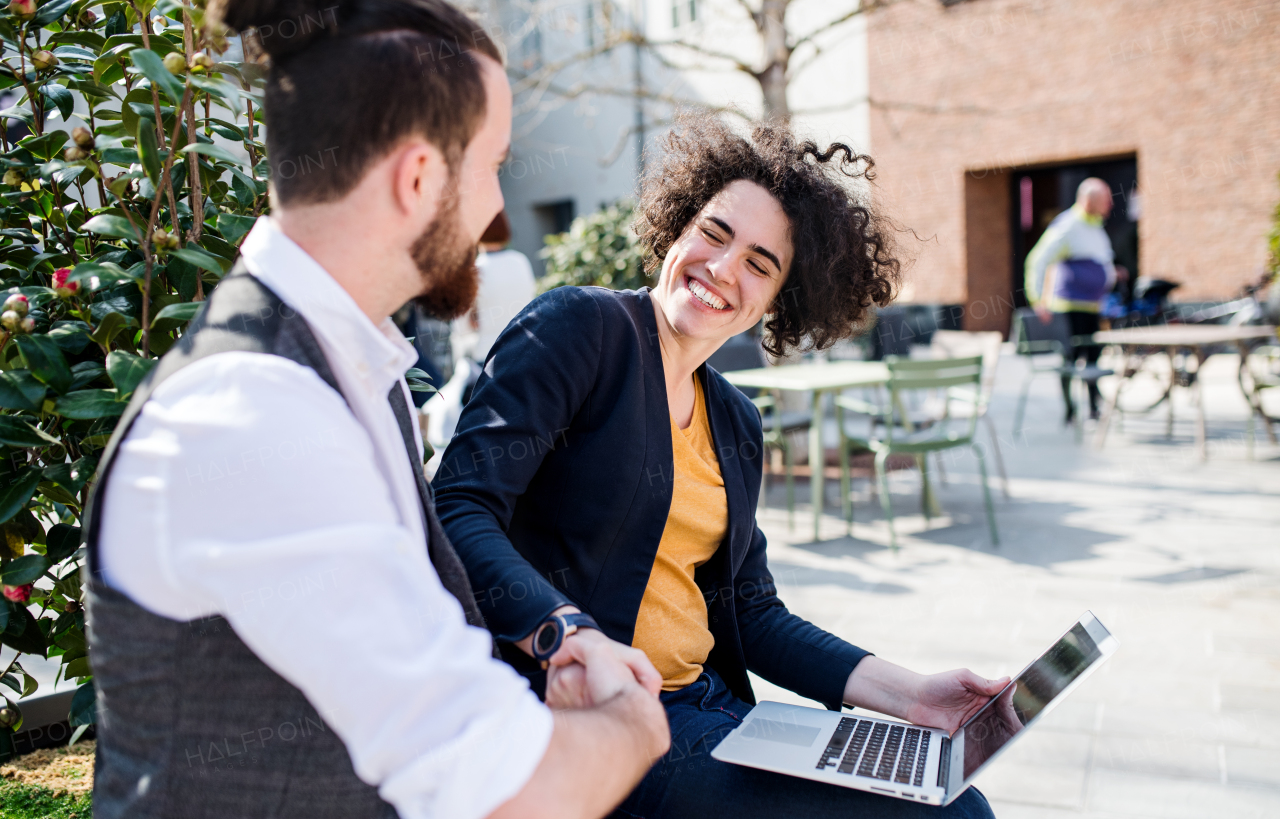 Young businesspeople with laptop outdoors in courtyard, expressing excitement. Start-up concept.