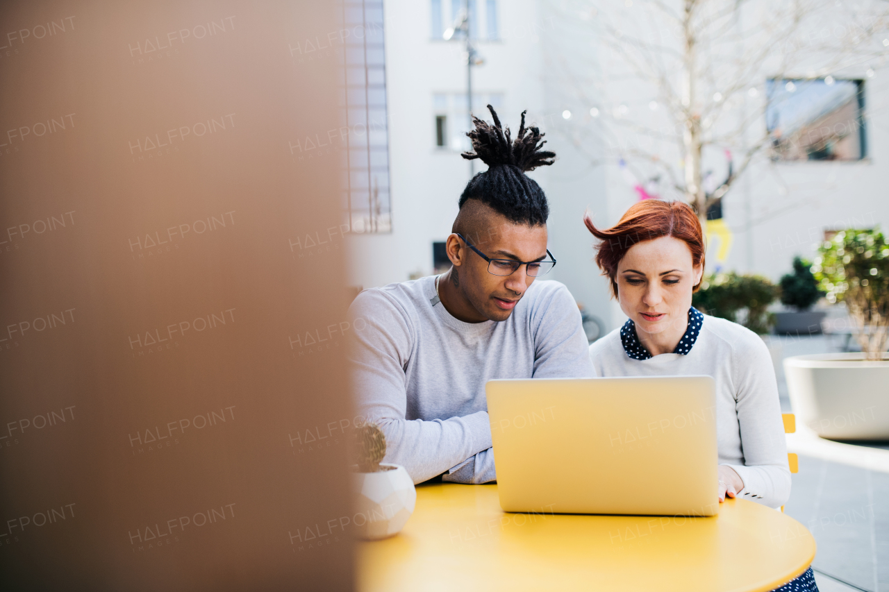 Young businesspeople with laptop outdoors in courtyard, talking. Start-up concept. Copy space.