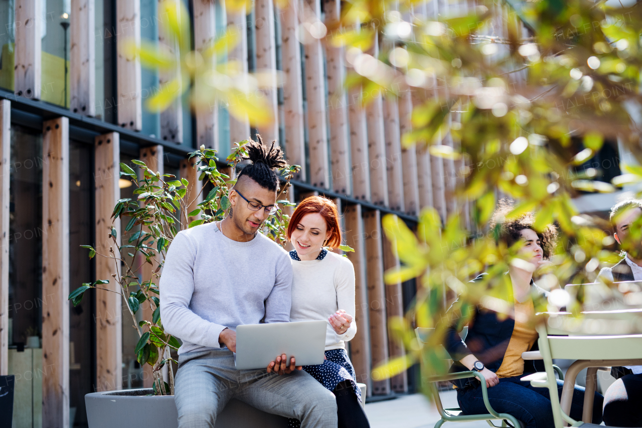 A group of young businesspeople using laptop outdoors in courtyard, start-up concept.