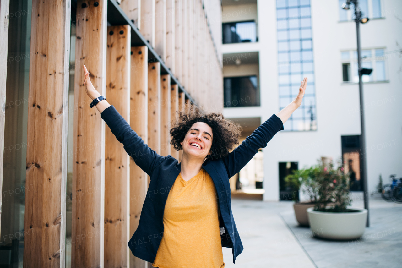 Young businesswoman standing outdoors in courtyard, expressing excitement. Start-up concept.