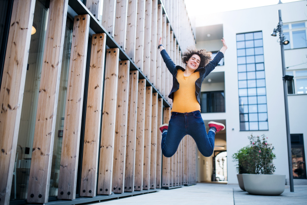 Young businesswoman jumping outdoors in courtyard, expressing excitement. Start-up concept.