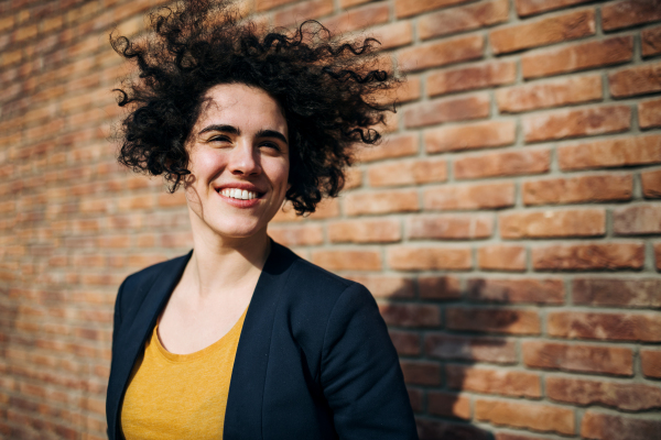 A happy young business woman standing outdoors, brick wall in the background. Start-up concept.