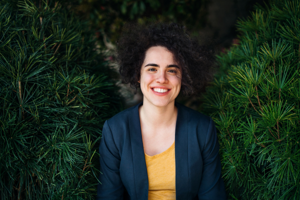 A young businesswoman standing outdoors against green background, looking at camera.