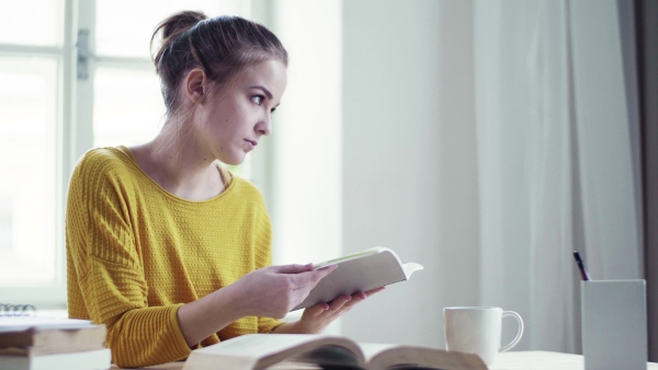 A young happy college female student sitting at the table at home, studying.