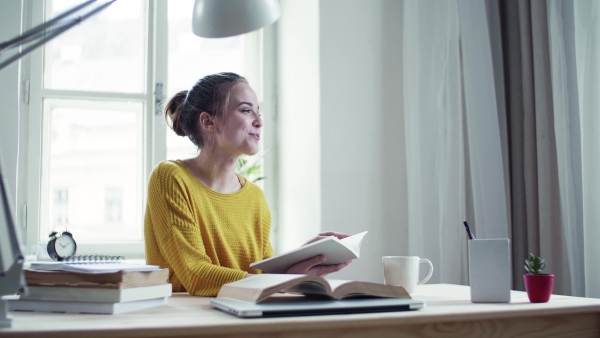 A young happy college female student sitting at the table at home, talking to somebody.