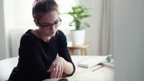 A young happy college female student sitting at the table at home, studying.