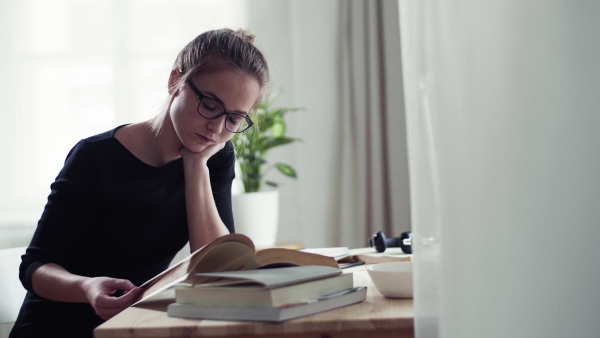 A young happy college female student sitting at the table at home, studying.