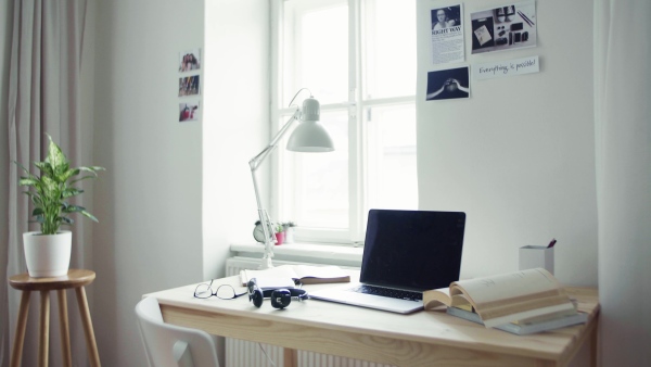 A desk with lamp, boks, headphones and laptop in a student room.