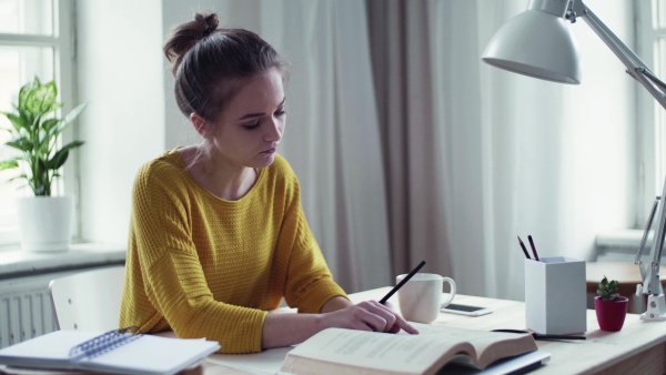 A young happy college female student with a book sitting at the table at home, studying.