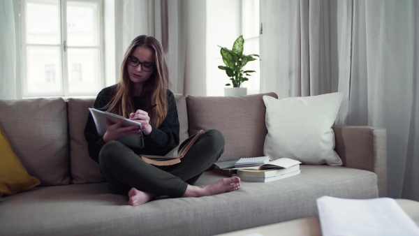 A happy young female student sitting on sofa, writing when studying.