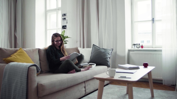 A happy young female student sitting on sofa, writing when studying.