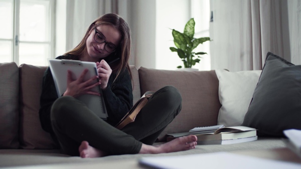 A happy young female student sitting on sofa, writing when studying.