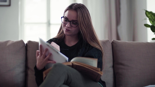 A happy young female student sitting on sofa, writing when studying.