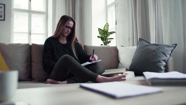 An unhappy, sad and frustrated female student sitting on sofa, studying.