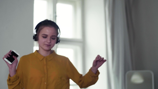 A young female student with headphones and telephone having a break when studying, dancing on sofa.