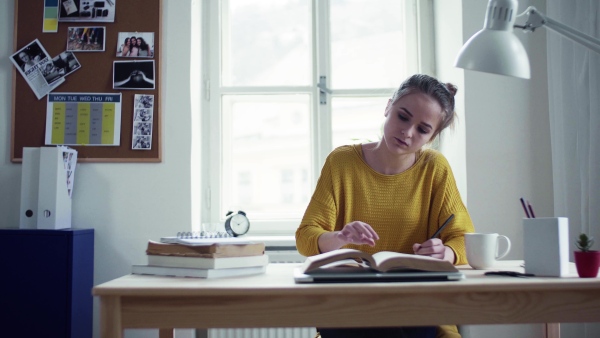 A young happy college female student with a book sitting at the table at home, studying.