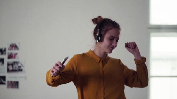 A young female student with headphones and telephone having a break when studying, dancing on sofa.