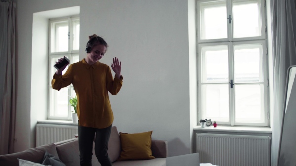 A young female student with headphones and telephone having a break when studying, dancing on sofa.