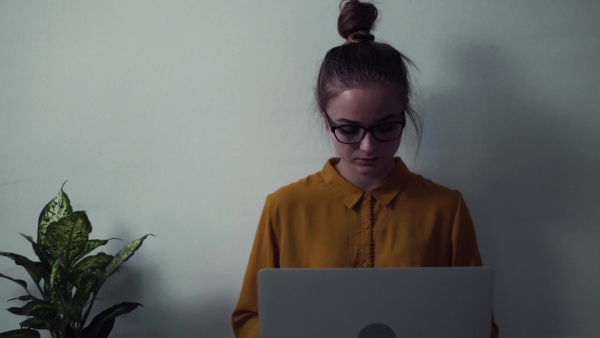 A young happy college female student with laptop sitting on floor at home, studying.