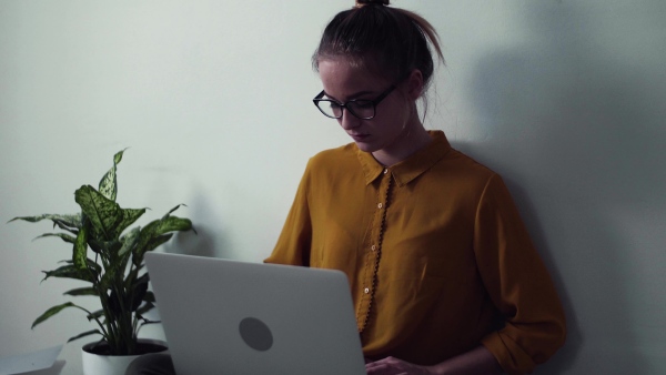 A sad young happy college female student with laptop sitting on floor at home, studying.