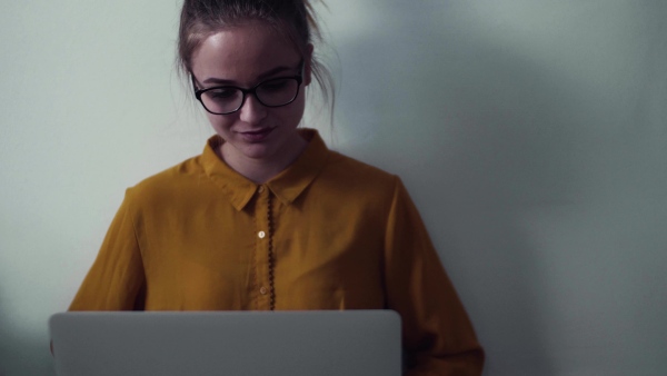 A young happy college female student with laptop sitting on floor at home, studying.