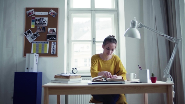 A young happy college female student sitting at the table at home, studying.