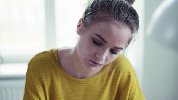 A young happy college female student sitting at the table at home, studying.