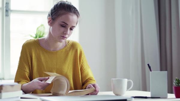 A young happy college female student with a book sitting at the table at home, studying.