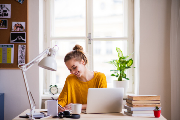 A young happy college female student sitting at the table at home, studying.