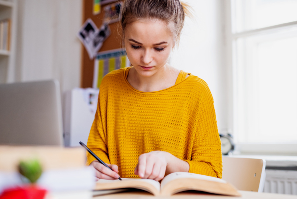 A young happy college female student sitting at the table at home, studying.