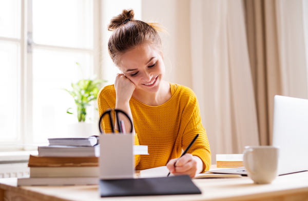 A young happy college female student sitting at the table at home, studying.